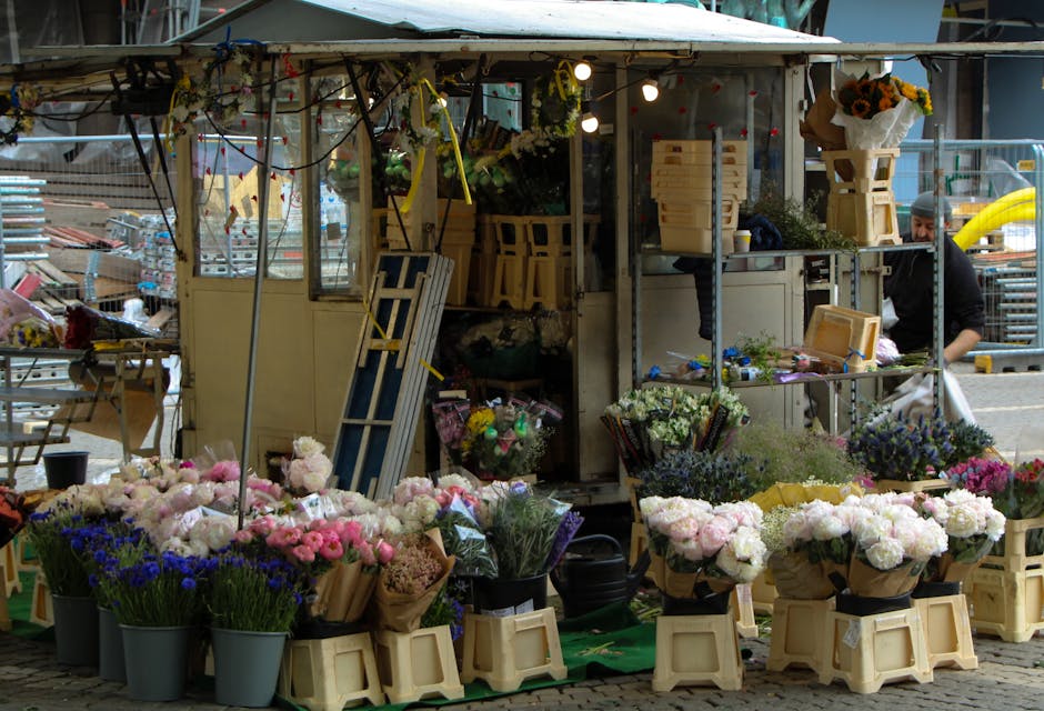 A flower stall at Northolt Road Market dedicated to floral arrangements and flower delivery, featuring an array of fresh flowers in various stages of arrangement. In the foreground, there are numerous